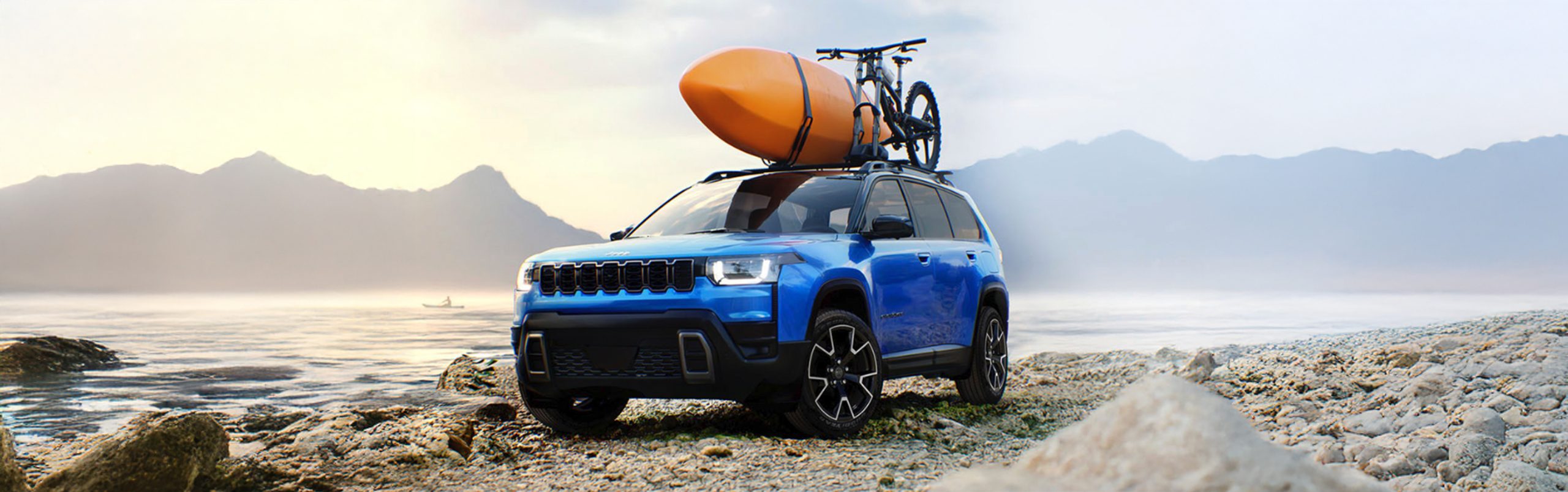 A blue 2026 Jeep Cherokee with a kayak and a bicycle on its roof rack is parked on a beach at dawn.